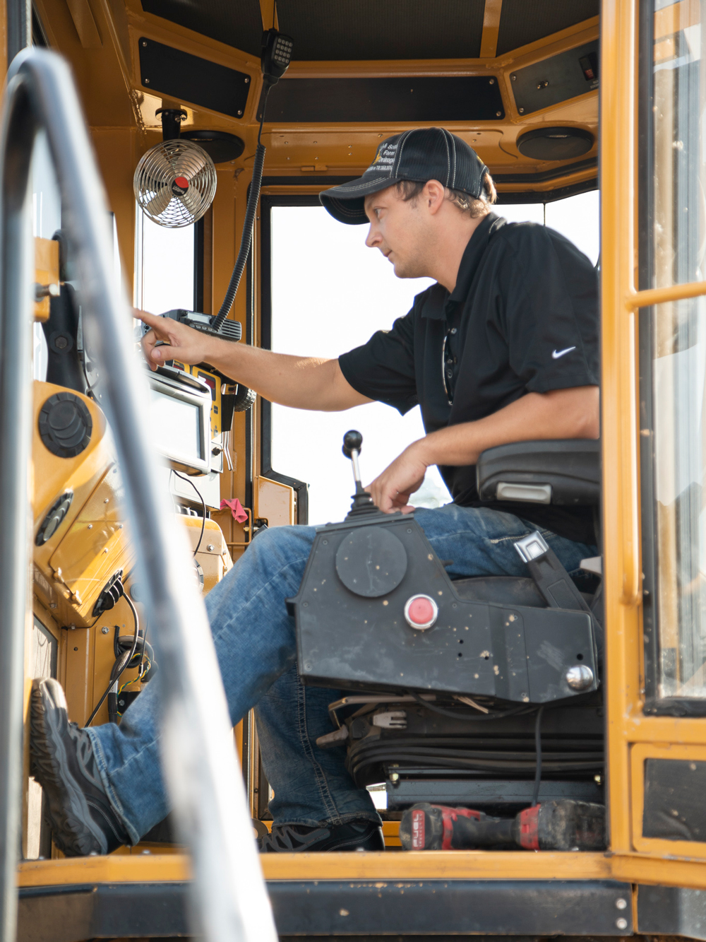 A Luft and Sons operator in a black shirt and cap is focused on maneuvering the controls inside the cab of a yellow trenching machine.